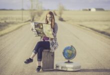 Giovane ragazza bionda legge una cartina seduta su una cassa di legno in mezzo a una strada nel deserto