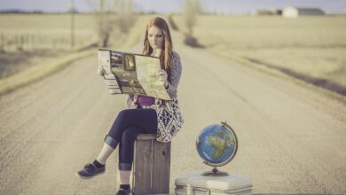 Giovane ragazza bionda legge una cartina seduta su una cassa di legno in mezzo a una strada nel deserto
