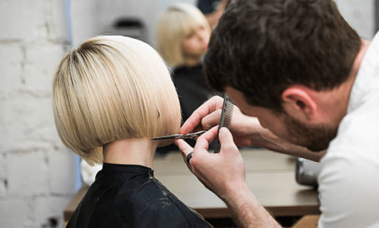 Parrucchiere taglia i capelli a una donna con il caschetto biondo