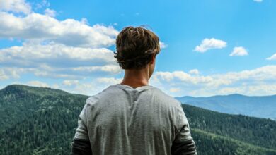 Giovane uomo di spalle ammira il panorama dalla cima di una montagna