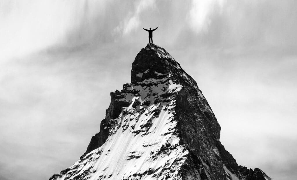 Arrampicatore in cima alla montagna con braccia verso il cielo