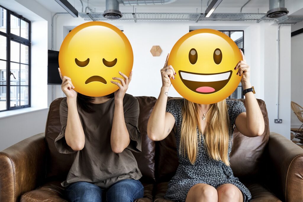 due donne sedute sul divano con emoji triste e sorridente al posto della testa