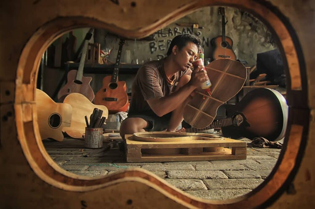 Giovane liutaio seduto a terra lavora circondato da pezzi di chitarre classiche