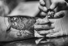 Tatuatore disegna un gufo sul braccio di un cliente