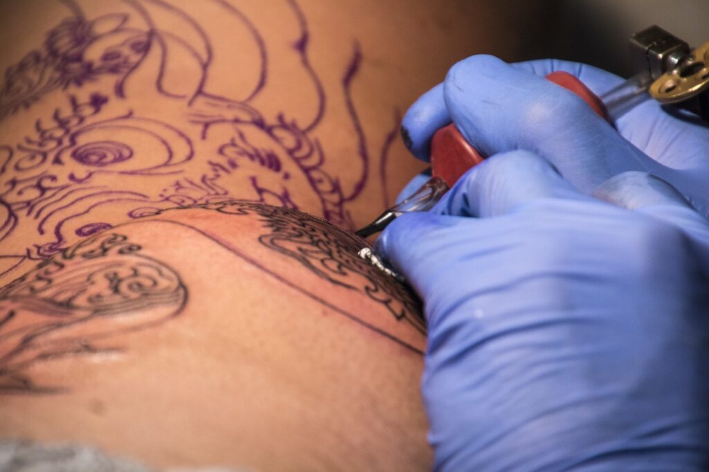 Tatuatore con guanti blu disegna un drago